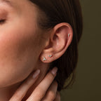Close up of a model wearing three dainty silver crystal flat back earrings in coordinating cluster designs for a minimalist ear stack.