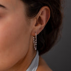 Close-up of a woman's ear wearing Duo Mirror Chain Huggies in Sterling Silver, featuring small dangling beads, set against a dark background—an elegant display of modern jewelry.