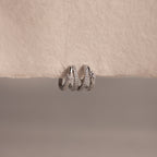 The Starburst Pave Duo Huggies in Sterling Silver rest on a textured, off-white surface, perfect for pairing with silver rings or gold hoops for a celestial-inspired look.