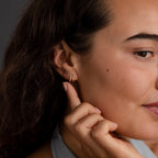 A woman gently touches her ear, showcasing the Starburst Pave Duo Huggies. Soft lighting highlights her face and the delicate celestial sparkle of these small gold earrings.
