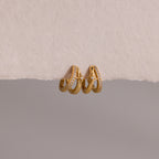 The Starburst Pave Duo Huggies feature two gold hoops—one with sparkling crystals, the other with a star charm—beautifully displayed on textured paper.