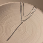 The Long Y Herringbone Chain Necklace in Silver is displayed on a textured, round beige ceramic plate with spiral patterns.