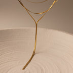 Inspired by the Long Y Herringbone Chain Necklace, this minimalist sculpture features thin gold wire extending from a textured white ceramic bowl, evoking elegant lariat-like lines in an abstract design.