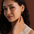 Model wearing gold huggie hoop earrings with dangling pave cross charms, stacked with dainty cross stud earrings.