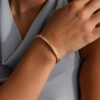 A person wearing a Ribbed Diamond Bangle in 18K Gold, adorned with small diamonds, paired with a light gray top.