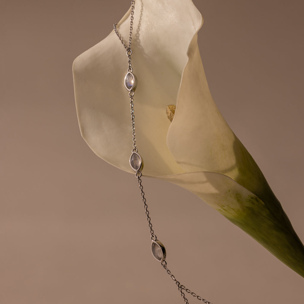 The Moonstone Hand Chain Bracelet in Silver, with its celestial charm, is gracefully displayed on a white calla lily set against a beige background.