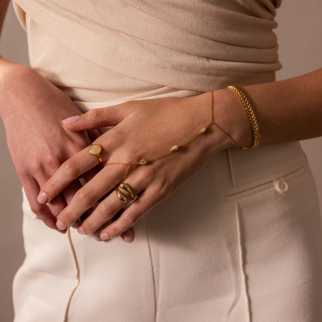 Woman wearing gold rings and the Moonstone Hand Chain Bracelet, styled with a cream top and side-button skirt.