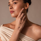 A woman in an off-shoulder top gazes thoughtfully to the side, showcasing the Moonstone Hand Chain Bracelet in Silver on her wrist.