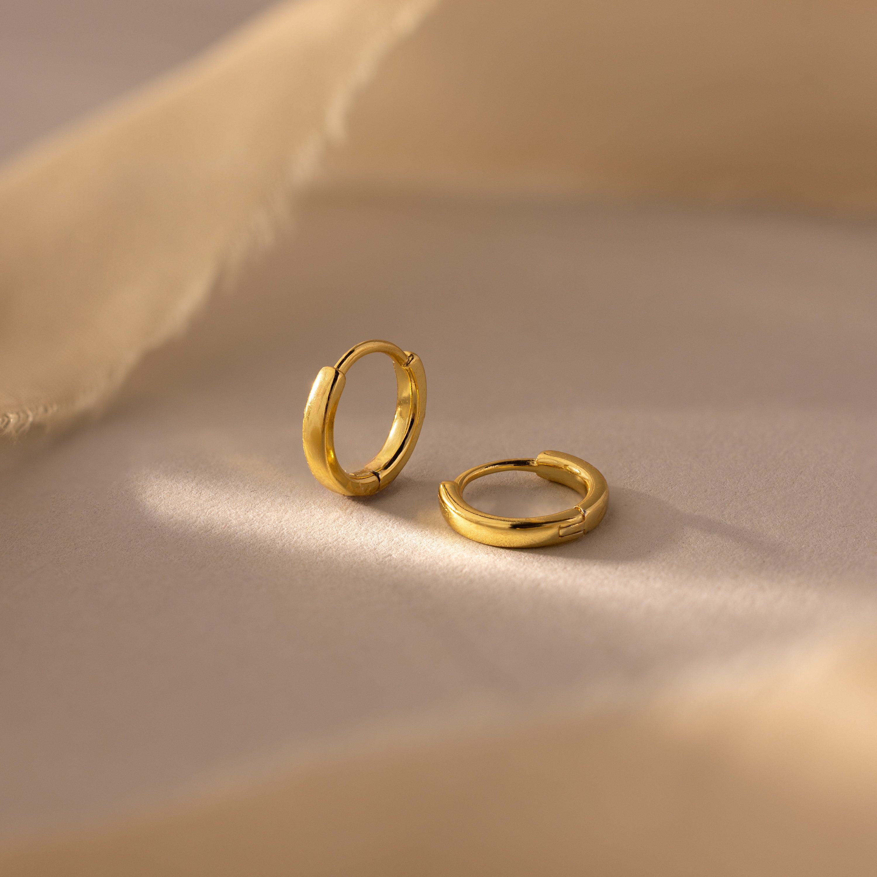 A pair of 7mm gold mini classic huggie hoop earrings displayed on a soft beige surface.