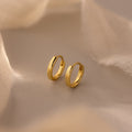 A pair of 7mm gold mini dainty huggie hoop earrings displayed on a soft beige fabric background with warm lighting.