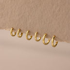 Set of 3 pairs of gold huggie hoop earrings in multiple sizes (6mm to 8mm) displayed on a neutral fabric.