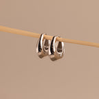 Close-up of a pair of polished silver oval-shaped huggie earrings hanging from a wooden rod.