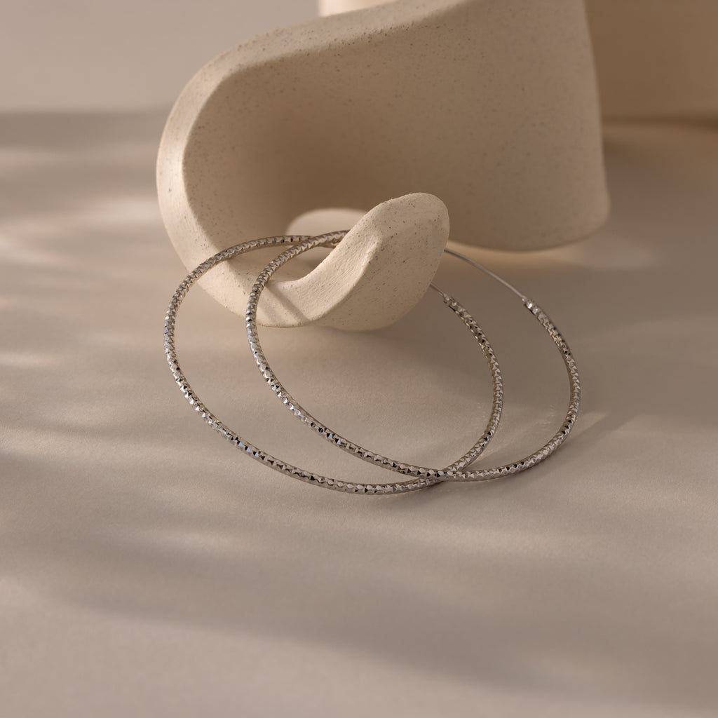 Large silver hoop earrings with a textured finish resting against a neutral-toned ceramic dish.