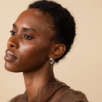 A woman with short curly hair wears the elegant Triple Knot Earrings in Silver and a sheer brown top—an ideal anniversary gift.