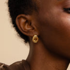 Close-up of a person’s ear wearing a single Mini Triple Knot Earring in polished 18K gold. The earring features three rounded loops interwoven into a compact knot shape that hugs the earlobe