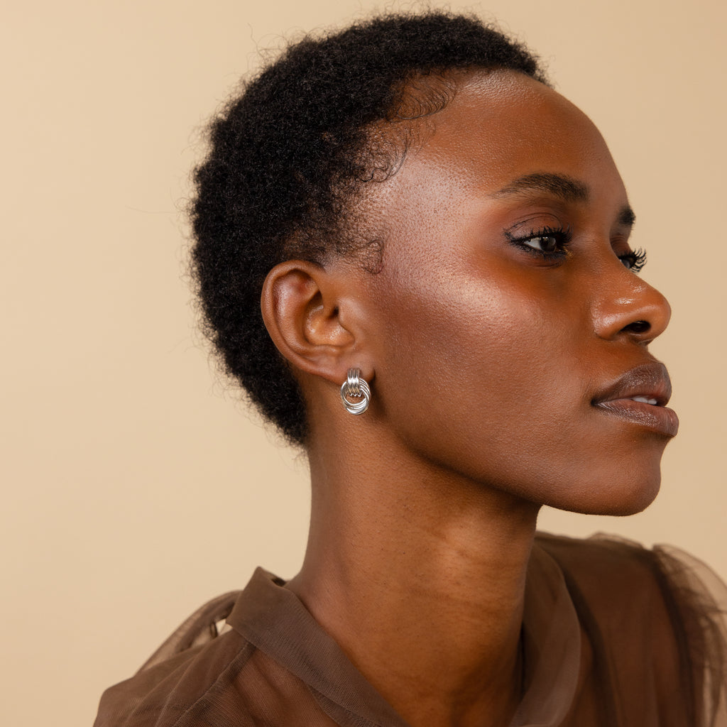 A woman wears the silver-toned Mini Triple Knot Earring on her earlobe