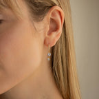 Close-up of a woman wearing Caroline Pave Drop Huggies—gold hoops with two dangling clear gemstones.