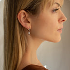 A woman with straight blonde hair wears Caroline Pave Drop Huggies against a neutral background, highlighting the elegance of these diamond earrings.