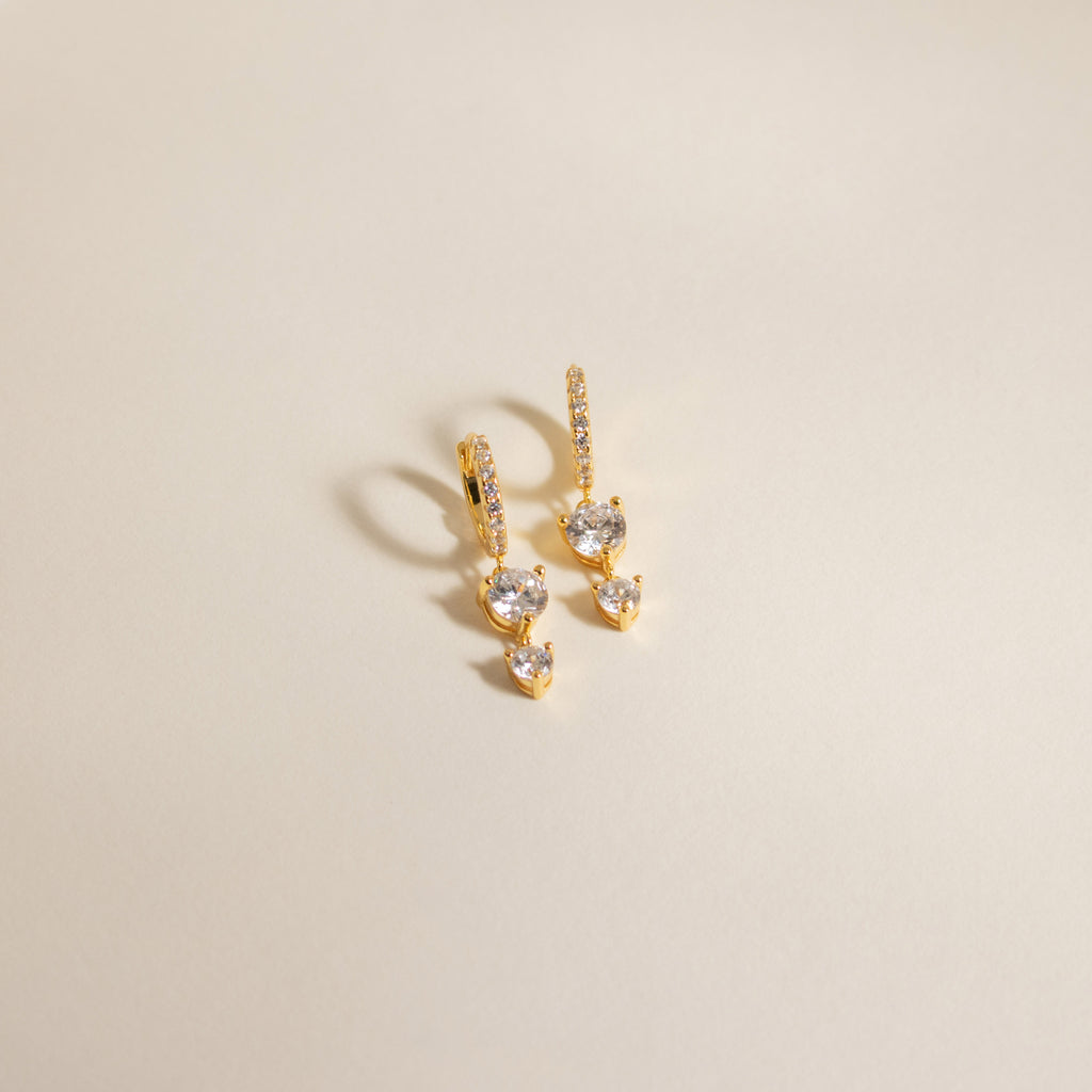 Caroline Pave Drop Huggies gold earrings with sparkling stones displayed on a neutral, light background.