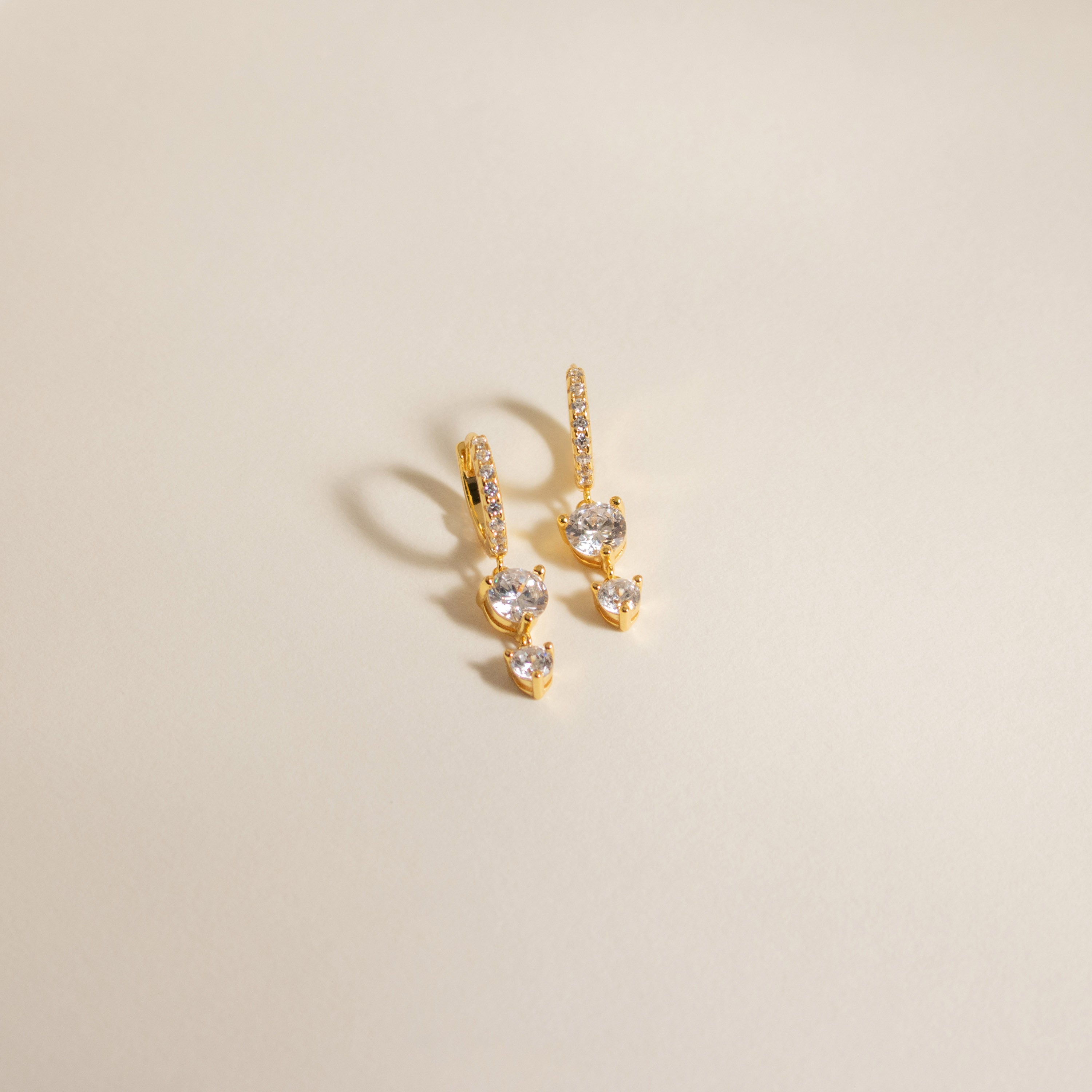 Caroline Pave Drop Huggies gold earrings with sparkling stones displayed on a neutral, light background.