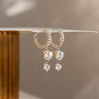 Caroline Pave Drop Huggies: sparkling gold hoops adorned with teardrop gems, showcased on a white surface.