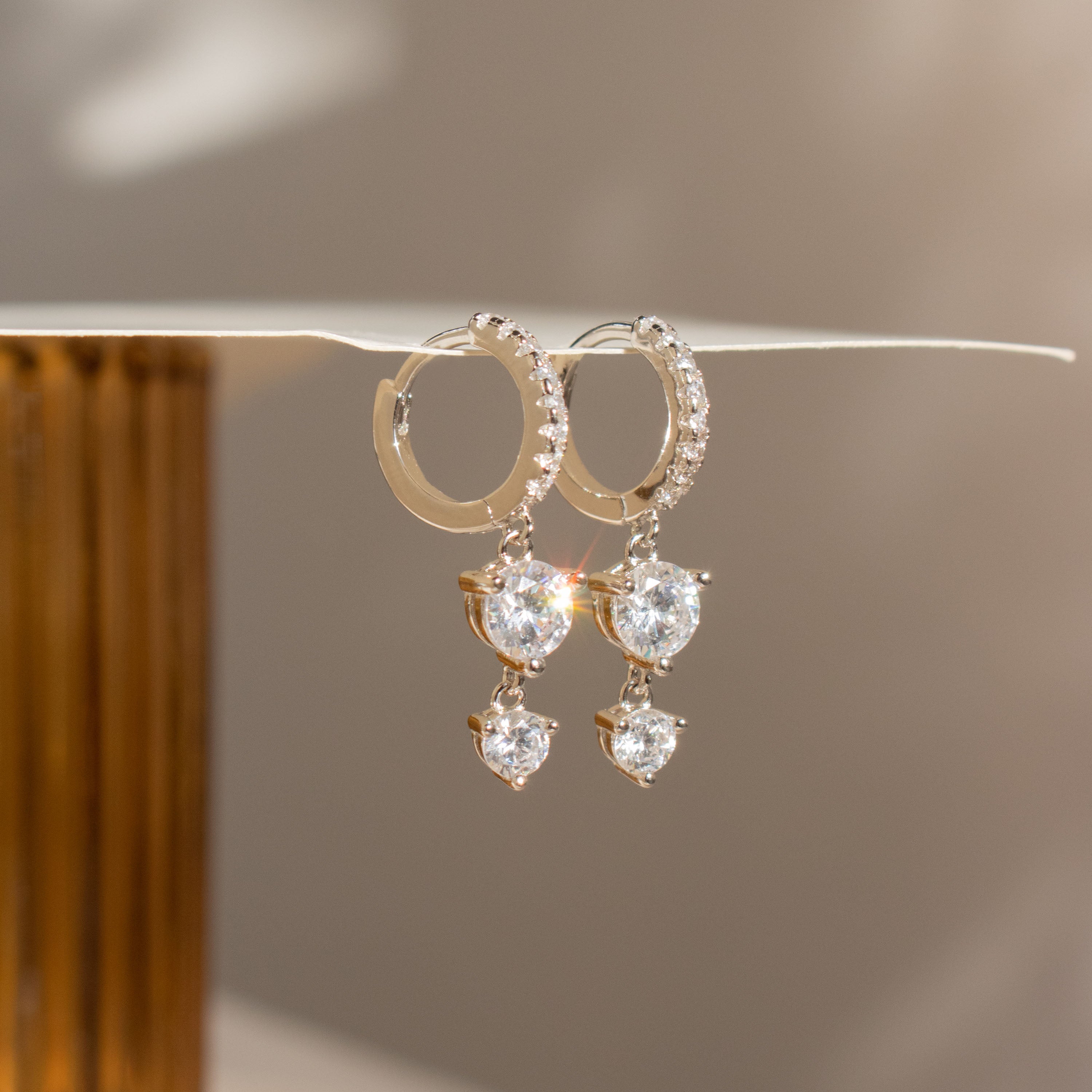 Caroline Pave Drop Huggies: sparkling gold hoops adorned with teardrop gems, showcased on a white surface.