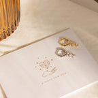 Caroline Pave Drop Huggies earrings rest on a card that says A NOTE FOR YOU, featuring a hand and heart illustration.