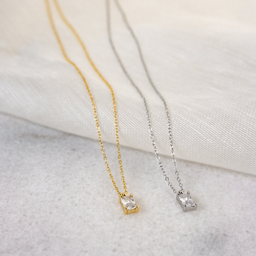 The Sage Diamond Necklace in Silver, featuring a delicate rectangular pendant, exudes timeless elegance against a light fabric background.