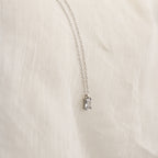The Sage Diamond Necklace in Silver features a delicate chain and rectangular gemstone pendant, radiating timeless elegance against a soft cream fabric background.