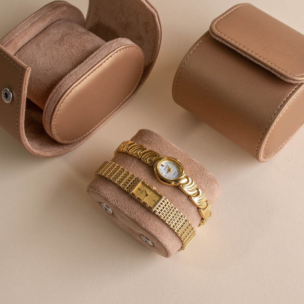 Two additional vintage-style gold watches displayed on a suede watch roll beside matching travel cases.