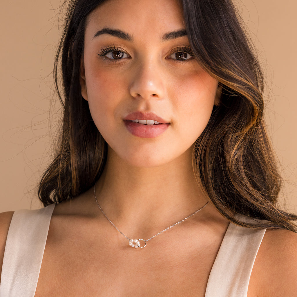 Woman with long brown hair wears a cream dress and an elegant Interlocking Pearl Necklace in Silver, looking at the camera.