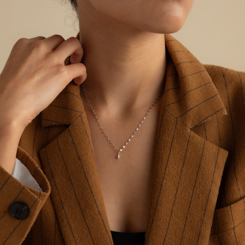 A woman in a brown pinstripe blazer wears the Dainty Marquise Pendant Necklace in Silver with a mirror twist chain, her hand resting gently near her neck.