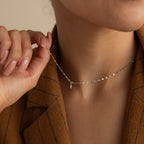 A person in a brown blazer holds the Dainty Marquise Pendant Necklace in Silver with a delicate mirror twist chain and a small marquise-shaped pendant near their neck.