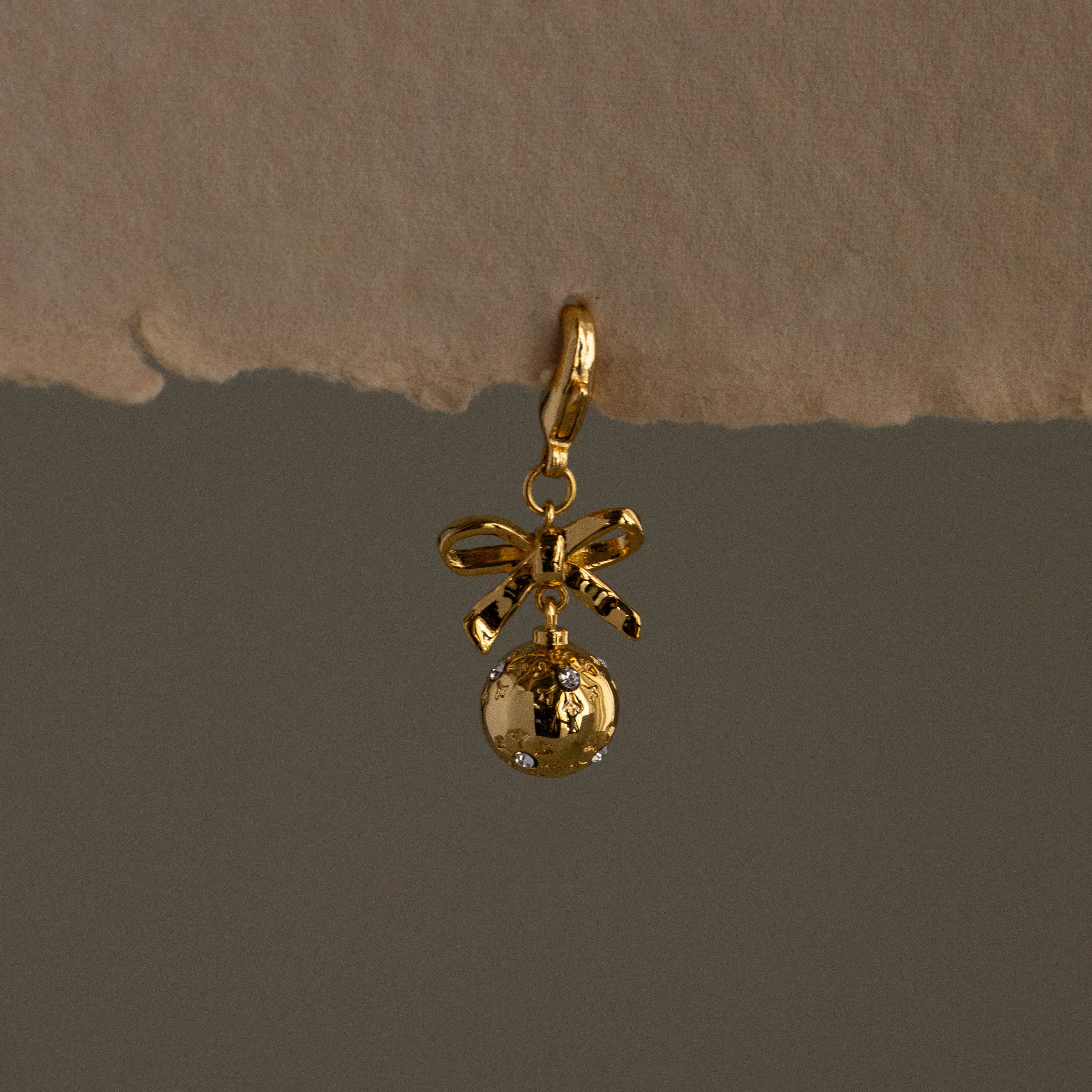 Pave Bow Ornament Charm featuring a bow and round charm with delicate details, displayed on a neutral background.