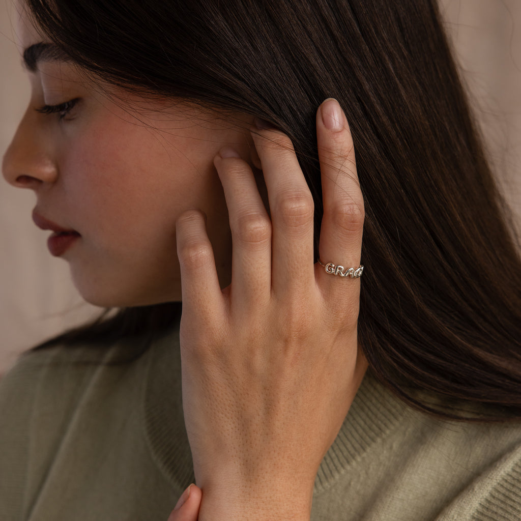 Model wearing a dainty silver bubble letter ring with the name "GRACE'.