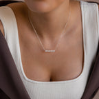 A woman wearing a Tiny Bubble Name Necklace personalized with BROOKE, dressed in a white top and brown jacket.