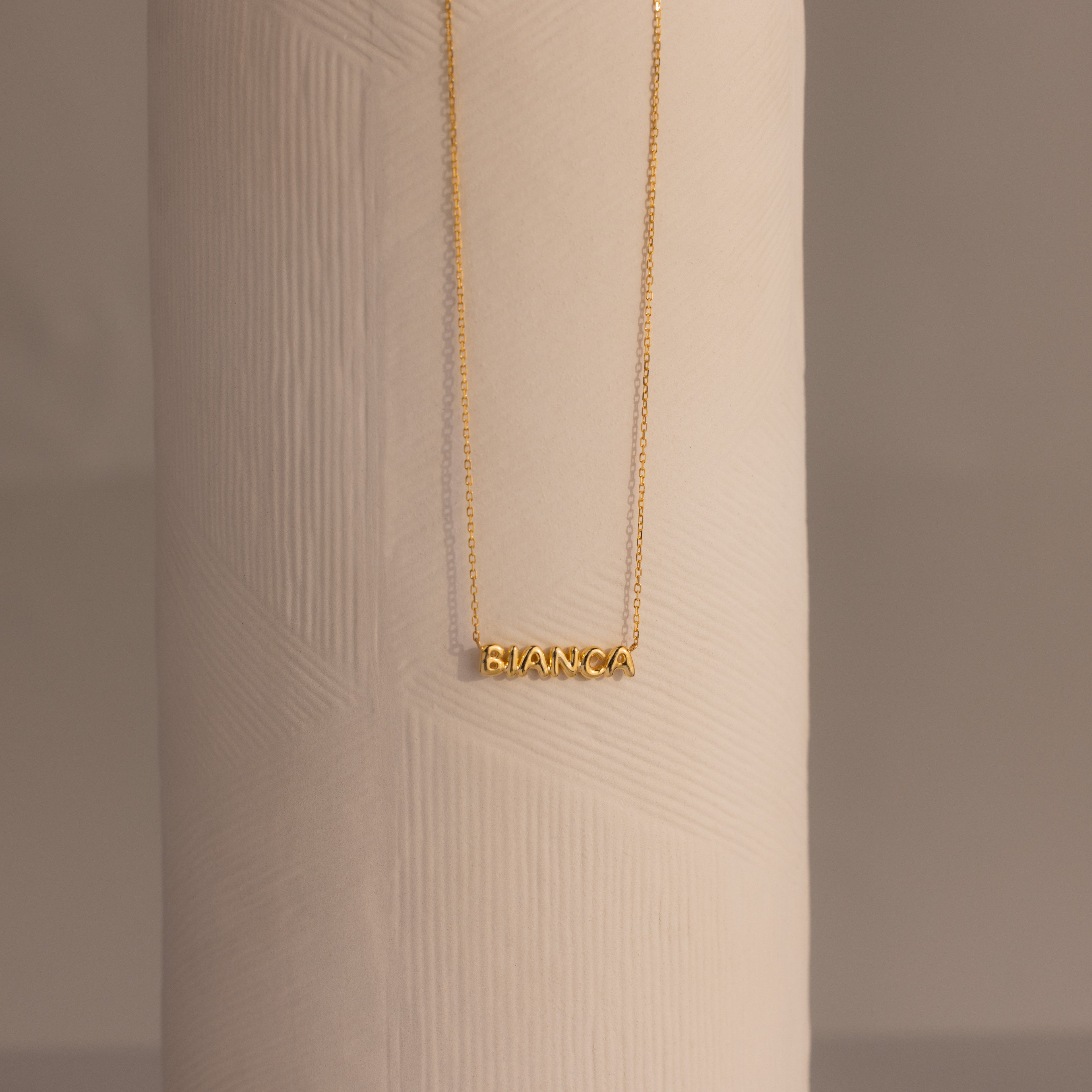 Tiny Bubble Name Necklace featuring BIANCA on a textured white cylinder—a personalized piece that adds a unique touch.