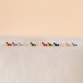 Bella Birthstone Studs—vivid, petite earrings arranged on a soft, neutral surface with a beige backdrop—make perfect personalized jewelry and a thoughtful gift for mothers and daughters.