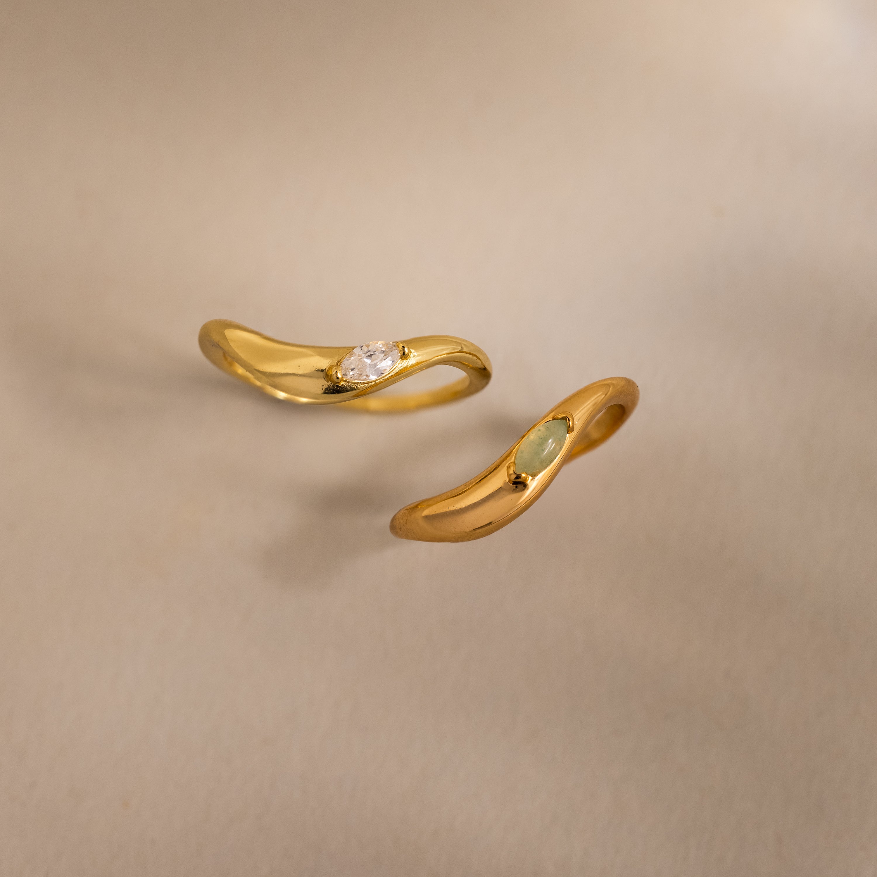 Two gold rings with sculpted bands and small gemstones are displayed on a neutral background, echoing the elegance of the Zen Jade Curve Ring.