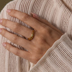 A hand wearing the Zen Gemstone Curve Ring in gold is placed on a cream-colored, textured knit sweater.