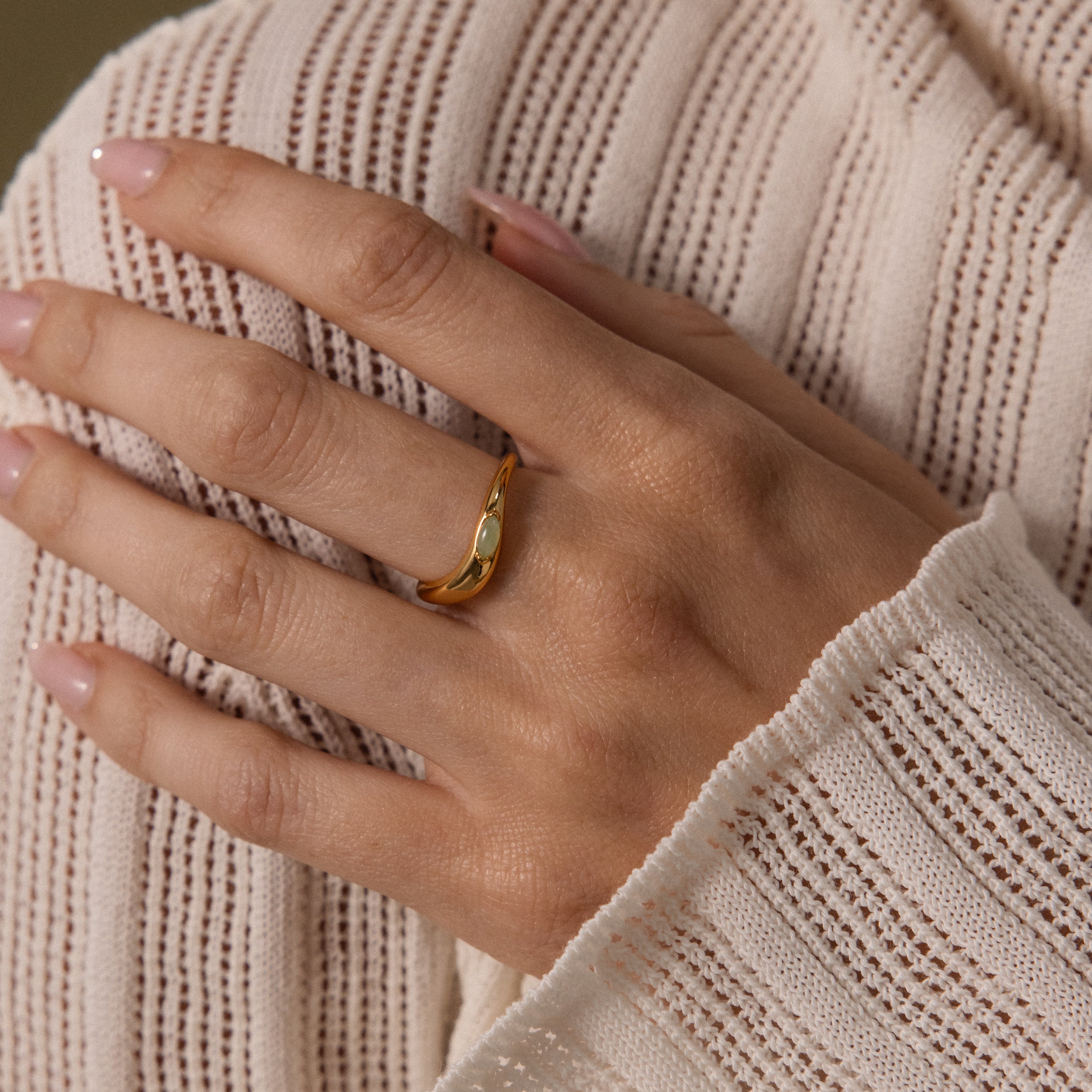 A hand wearing the Zen Gemstone Curve Ring in gold is placed on a cream-colored, textured knit sweater.