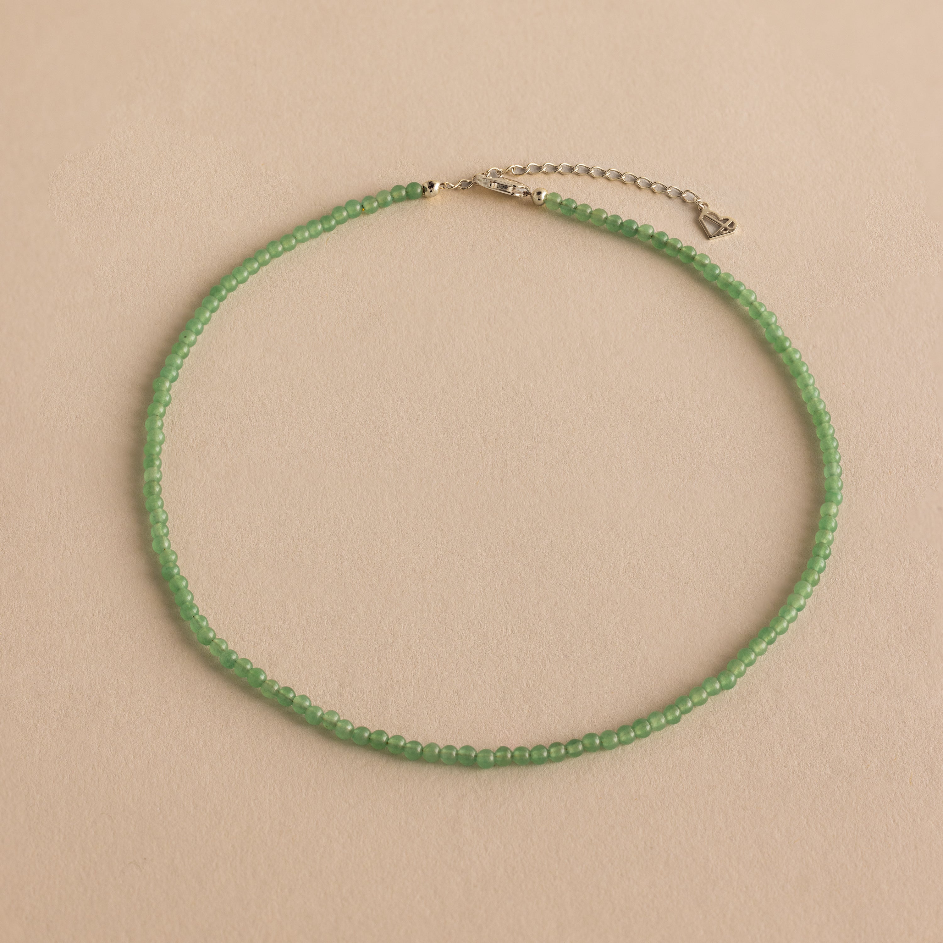 The Tiny Jade Choker Necklace in Silver features delicate green jade beads and a silver clasp with extender, shown on a beige background.