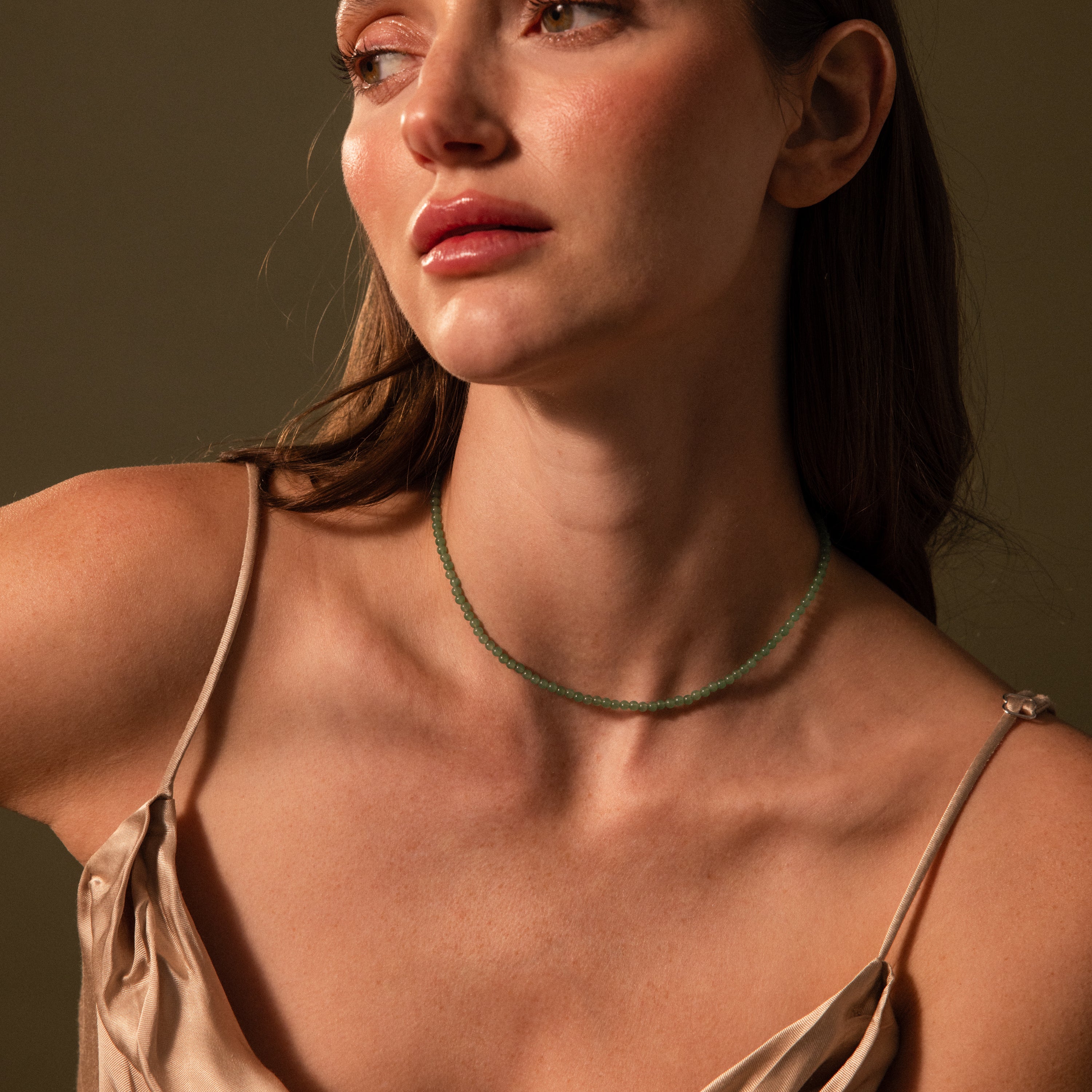 Woman in a satin dress wearing the Tiny Jade Choker Necklace, featuring delicate jade beads, looking to the side against a neutral background.