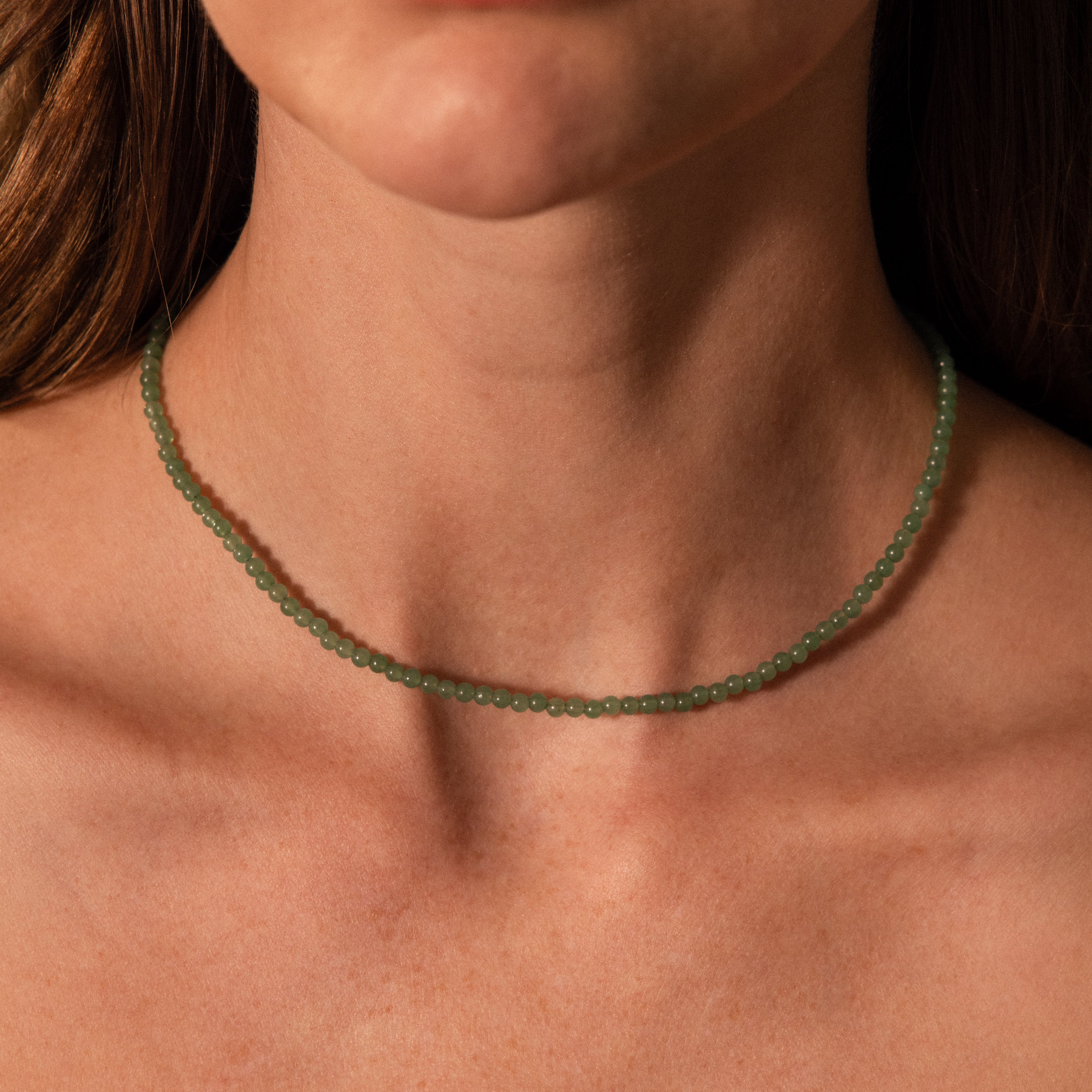 Close-up of a woman's neck wearing the Tiny Jade Choker Necklace in Silver, featuring green jade beads against bare skin.