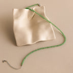 The Tiny Jade Choker Necklace in Silver, featuring green jade beads, is displayed on a draped cream ceramic tray set against a beige background.