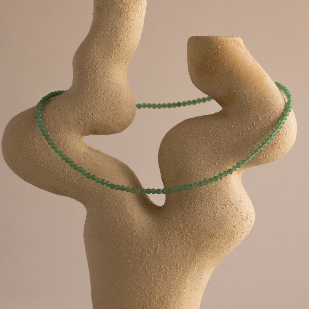 A stone sculpture adorned with a layered necklace featuring the Tiny Jade Choker Necklace in 18K Gold.