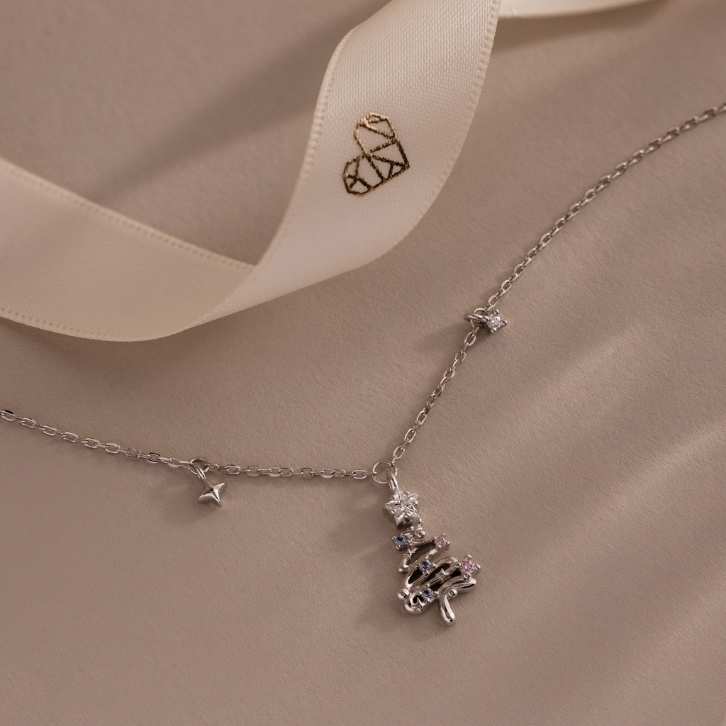 Flatlay of our Holiday Diamond Tree Necklace on a beige background with a Caitlyn Minimalist logo ribbon