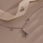 Flatlay of our Holiday Diamond Tree Necklace on a beige background with a Caitlyn Minimalist logo ribbon