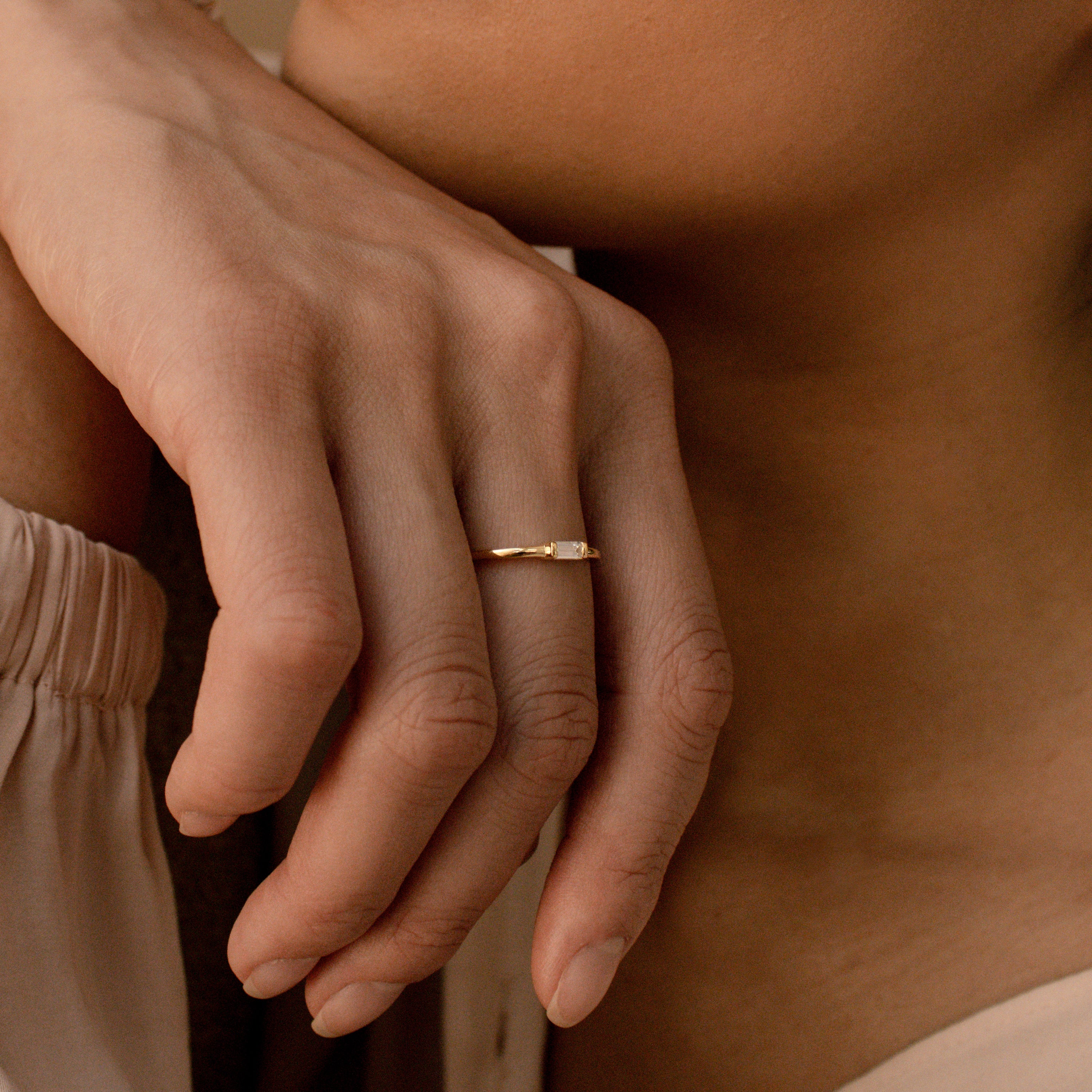 A close-up of a hand wearing the Baguette Diamond Ring in Silver, showcasing a dainty baguette diamond set in an elegant east-west bezel setting.