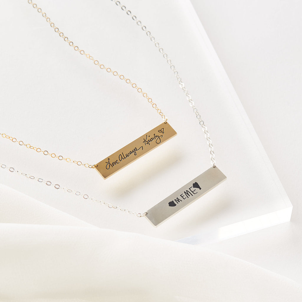 Two gold and silver bar necklaces with engraved text on a white background